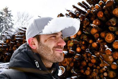 Close-up of smiling man wearing cap against logs