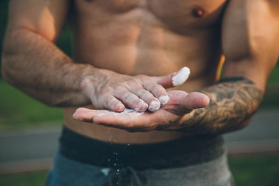 Midsection of shirtless man applying chalk on hand whiles standing outdoors