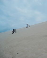 Low angle view of men carrying bicycle while walking on sand dune at desert