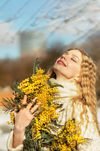 Portrait of a young woman with blond hair holding a bouquet of mimosa in her hands. spring.