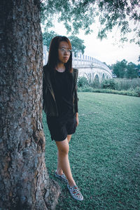 Woman standing by tree trunk against plants