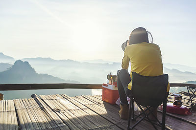 Rear view of man sitting on wood against sky