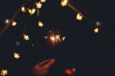 Cropped hand with sparkler burning at night