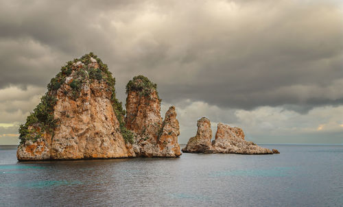 Scenic view of sea and rocks against cloudy sky