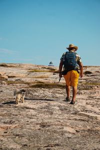 Rear view of man walking with dog on rock formation against sky