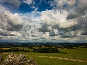 Scenic view of green landscape and mountains against cloudy sky