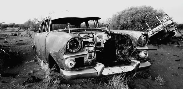 Abandoned car on field against sky