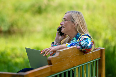 Senior woman at the garden working from home using laptop and speaking on the phone