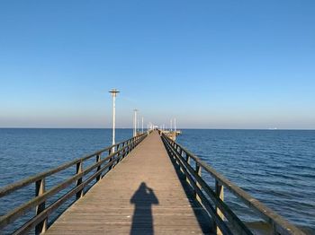 Pier over sea against clear blue sky