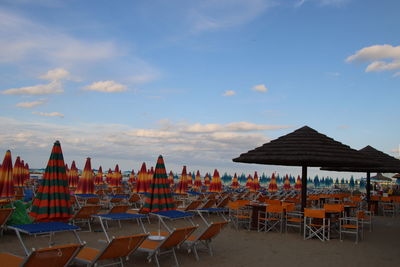 Empty chairs and tables on beach against sky
