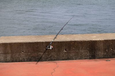 High angle view of fishing rod on promenade retaining wall against sea