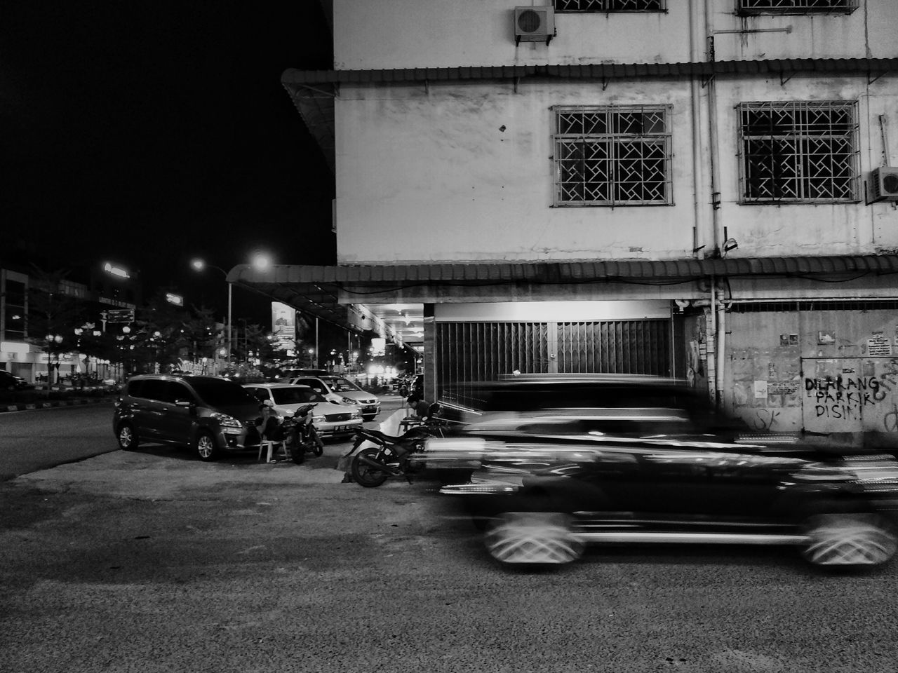 CARS ON ROAD BY BUILDINGS AT NIGHT