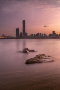 Sea by buildings against sky during sunset