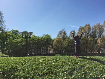 Full length of girl standing with arms raised at park against sky