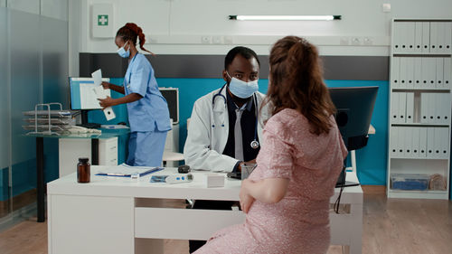 Doctor wearing mask examining pregnant woman at clinic