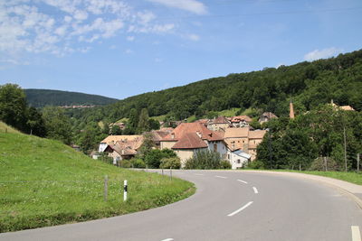 Road amidst buildings and mountains against sky