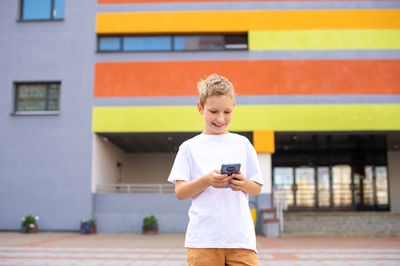 A boy is standing on the street with a phone