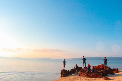 People on rocks at beach against sky