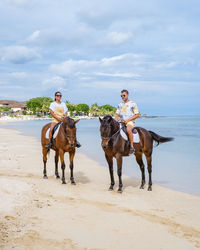 Man and woman riding horse at beach