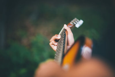 Cropped hand of person playing guitar over field
