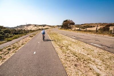 Rear view of women riding bicycle on road against sky