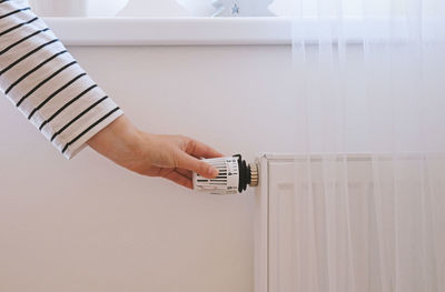 Woman regulates temperature at home with the heating thermostat to save energy, close-up with hand. 