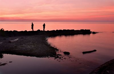 Silhouette people on rock by sea against sky during sunset