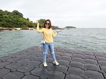 Portrait of smiling young woman standing in sea against sky