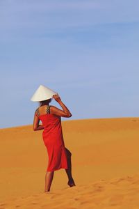 Woman with umbrella on desert against sky