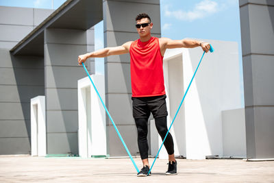 Full length of young man exercising with strap against built structure