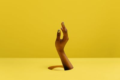 Close-up of woman hand against yellow background