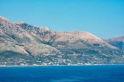 Scenic view of sea and mountains against clear blue sky