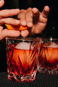 Cropped hands of person squeezing orange peel in cocktail on table