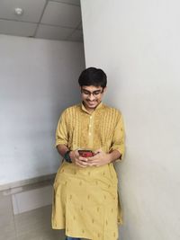 Young man in traditional clothing using mobile phone while standing against wall