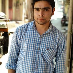 Portrait of young man in checked pattern shirt standing at city