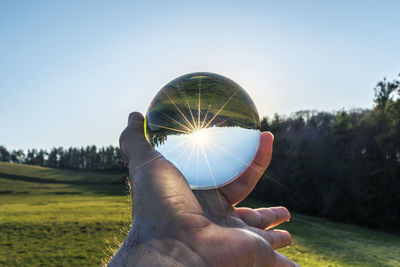 Cropped hand of person holding crystal ball against sky