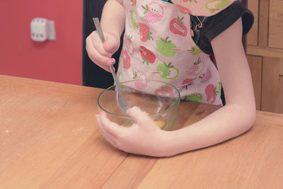 Midsection of girl preparing egg on table at home