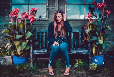 Young woman sitting on bench amidst flower pots