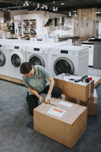 Female sales clerk opening cardboard package while working in appliances store