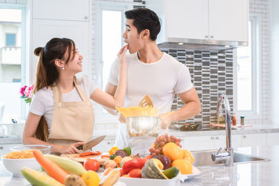 Woman feeding food to man in kitchen at home