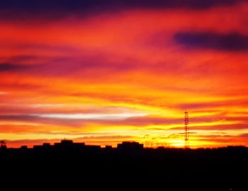 Silhouette of communications tower against orange sky
