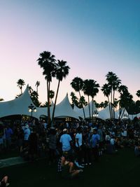 View of people gathered by tent and palm trees against sky at dusk