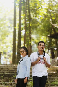 Smiling young woman standing by trees in forest