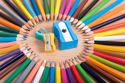 Close-up of sharpeners amidst colored pencils arranged on wooden table