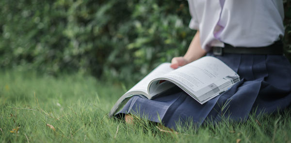 Midsection of woman reading book in field