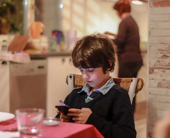 Boy using phone while sitting on chair at home