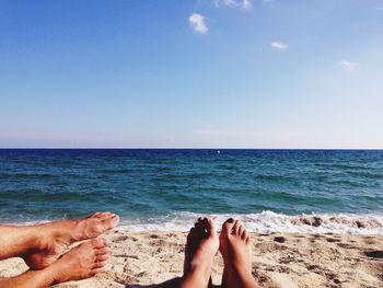 Low section of people on beach against blue sky