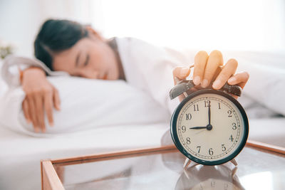 Close-up of alarm clock on table by woman sleeping on bed at home