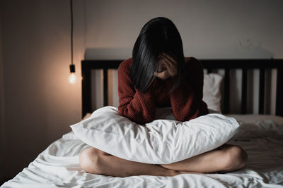 Sad young woman sitting on bed at home