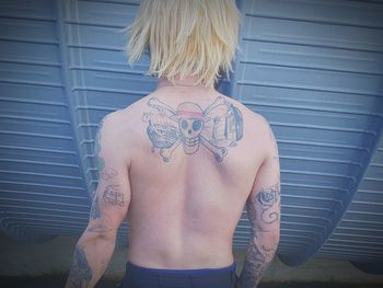 Rear view of shirtless tattooed man standing by blue structure